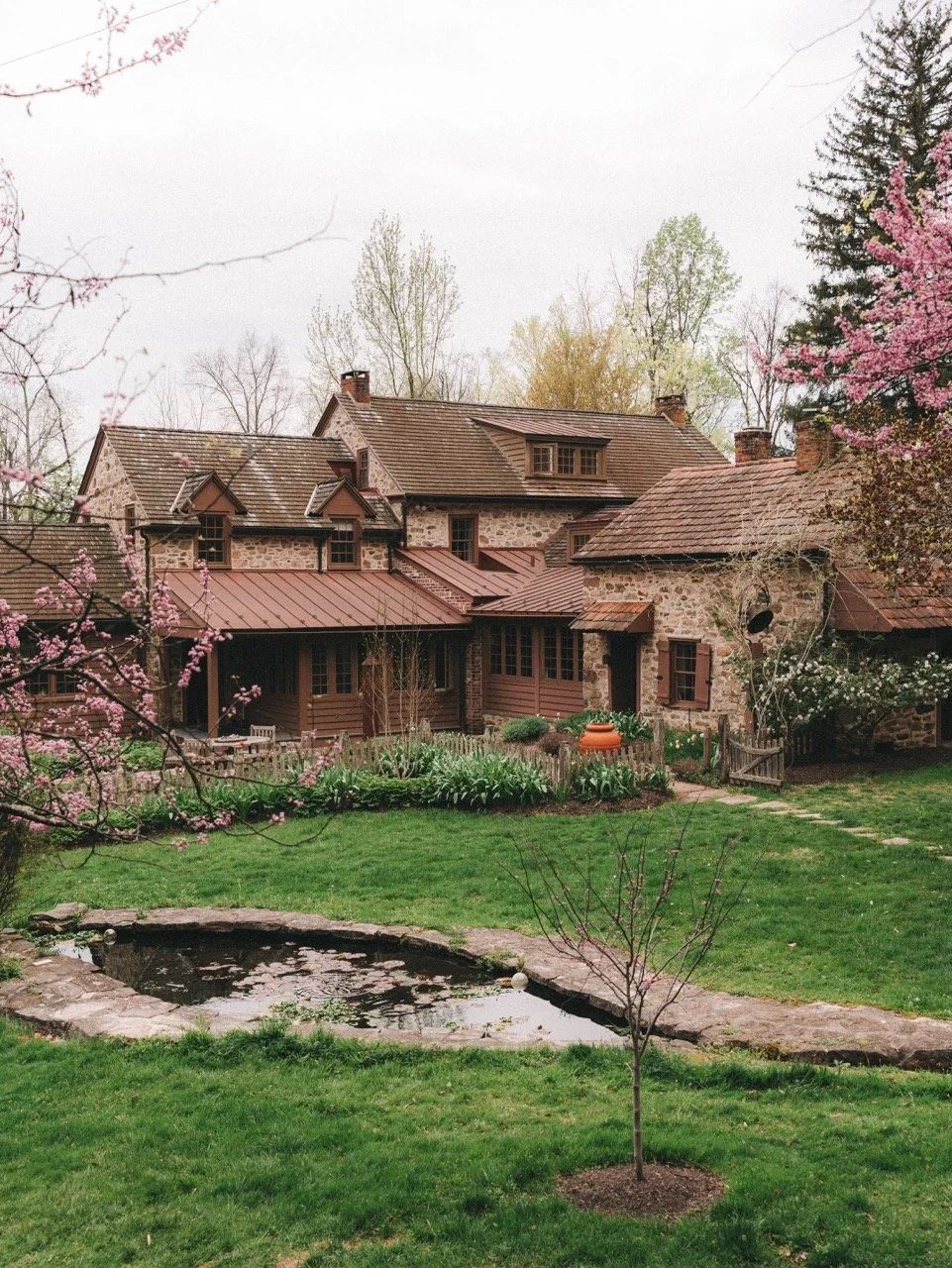 The stone farmhouse behind a pond, with blossoming trees on the lawn