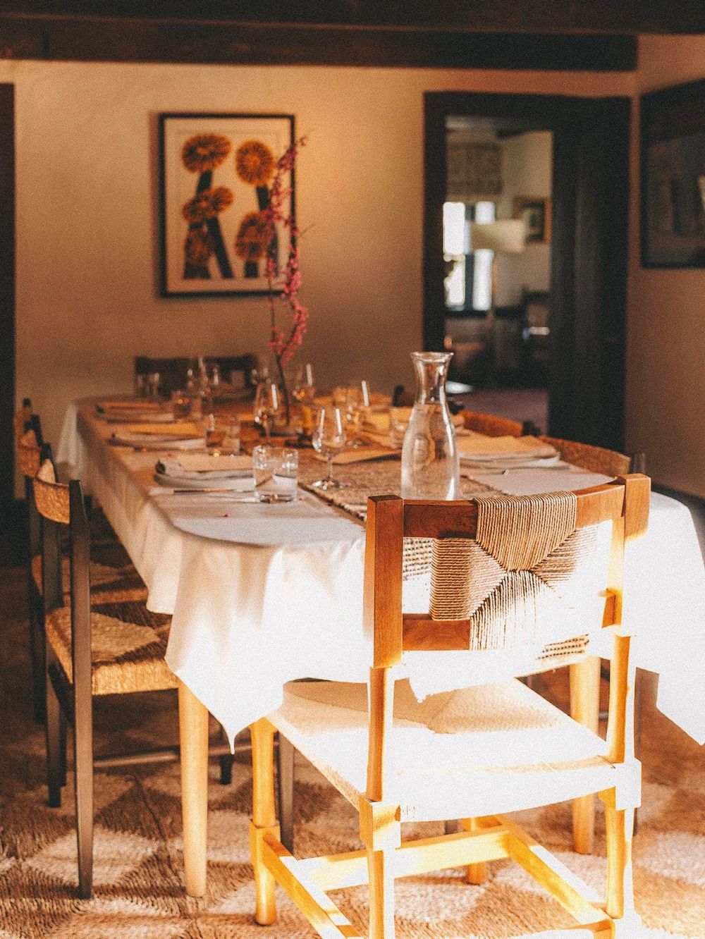 A long dining table set with linen and glassware in a sunlit room