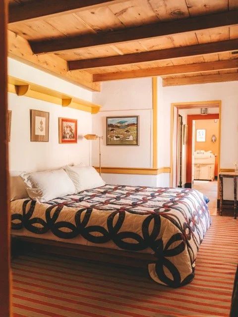 A bedroom with a patterned quilt beneath exposed wooden beams