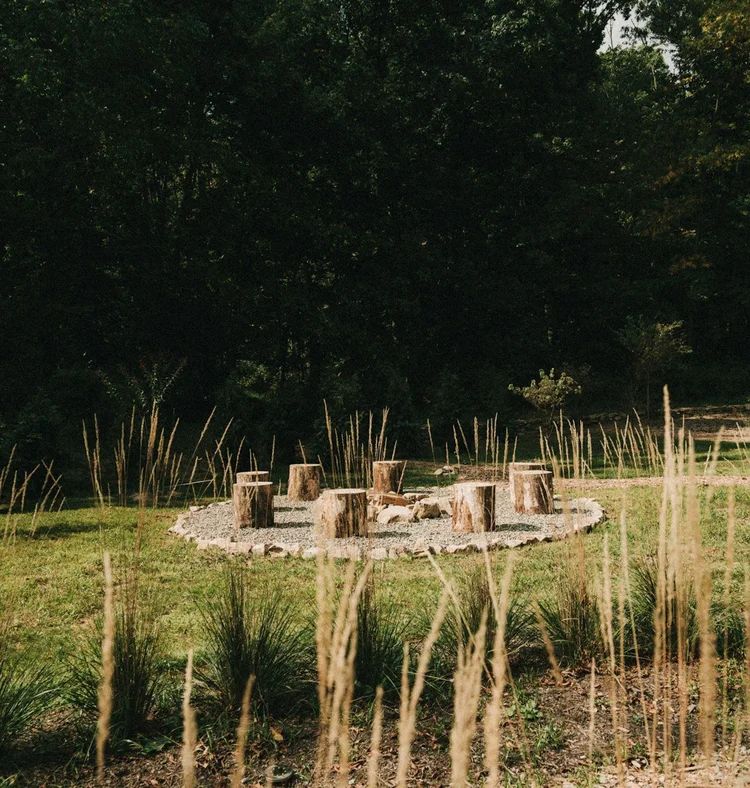 A ring of log seats around a firepit in tall grass