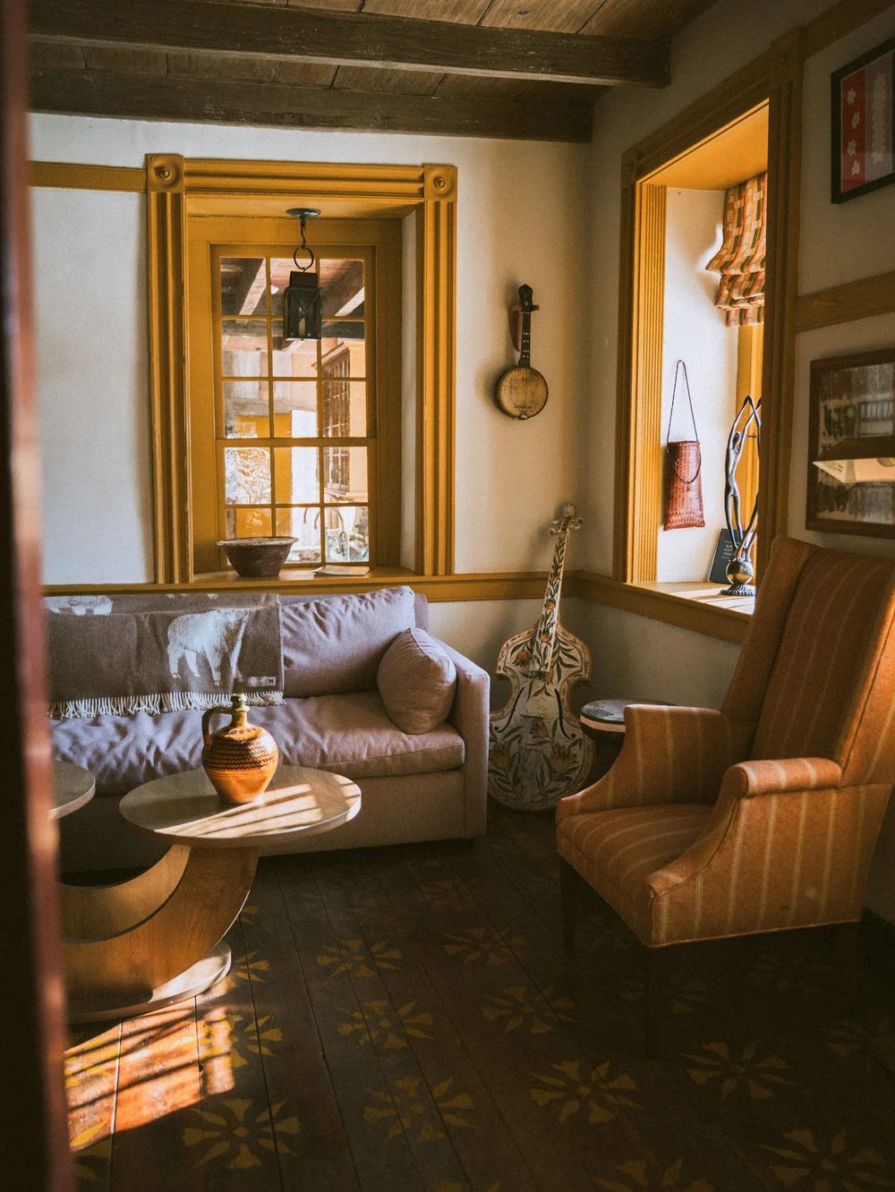 A sitting room with a sofa, a guitar and tall yellow-framed windows