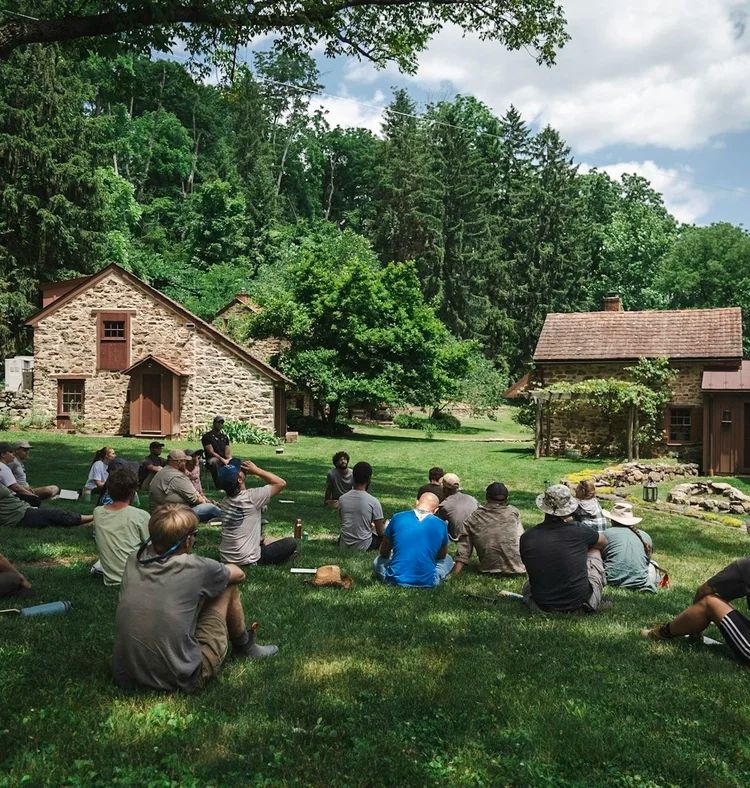 A group sitting together on the grass in front of a stone barn