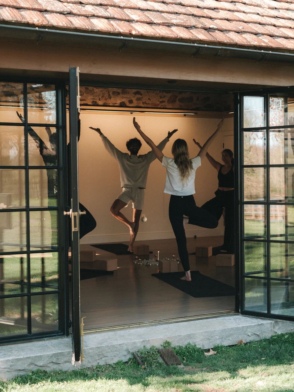 Two people in tree pose in a studio with its doors open to the outside
