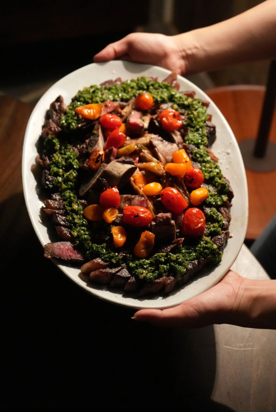 Hands holding a bowl of greens and roasted tomatoes